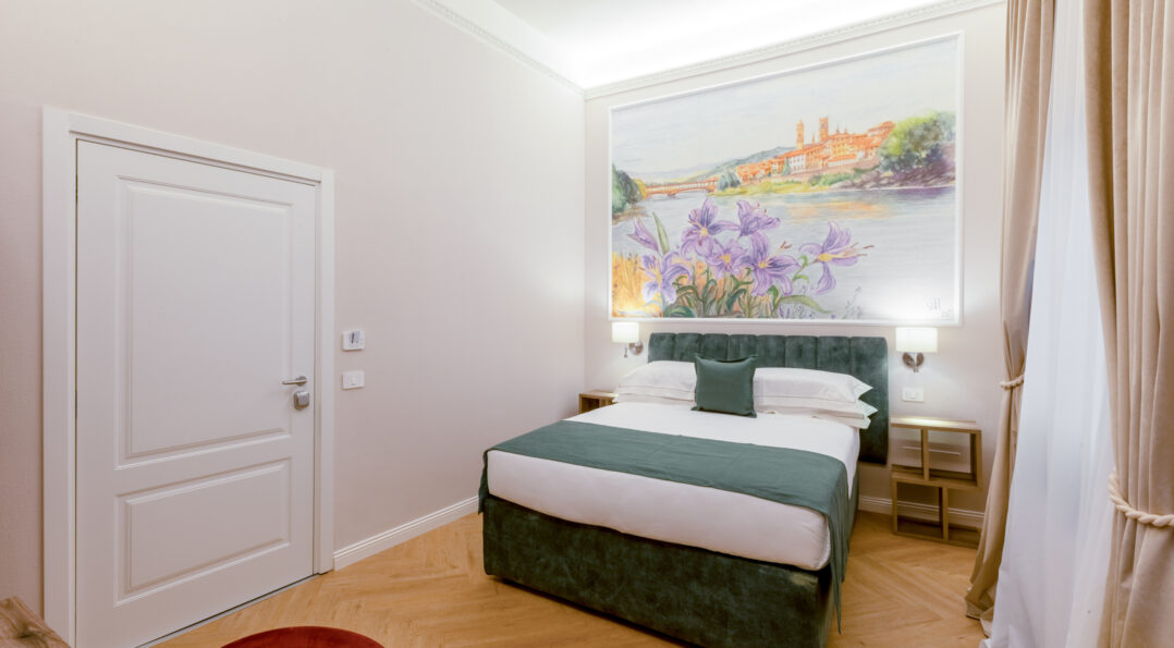 Camera matrimoniale Iris con letto verde, affresco floreale con iris e vista sull’Arno, parquet chiaro e tende color sabbia.