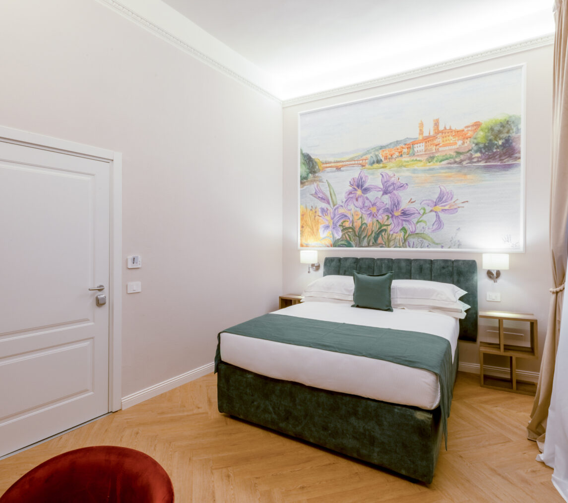 Camera matrimoniale Iris con letto verde, affresco floreale con iris e vista sull’Arno, parquet chiaro e tende color sabbia.
