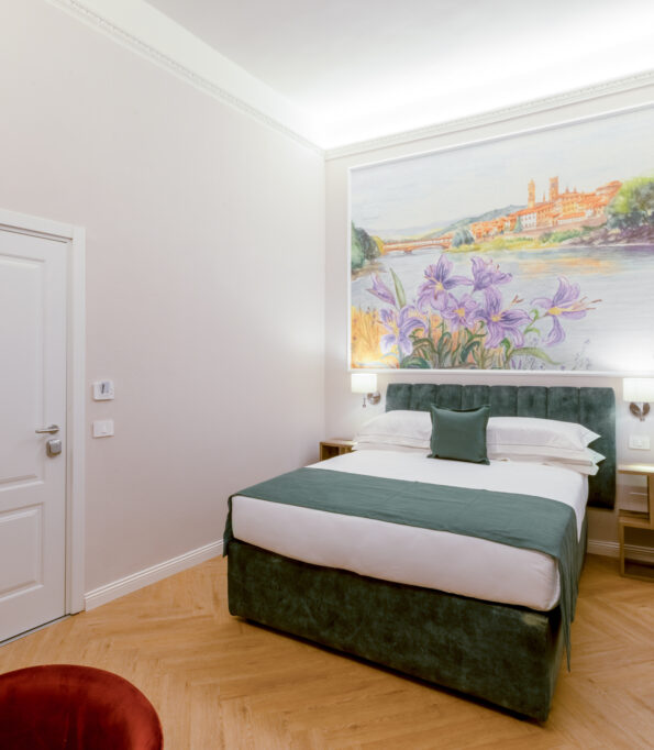 Camera matrimoniale Iris con letto verde, affresco floreale con iris e vista sull’Arno, parquet chiaro e tende color sabbia.