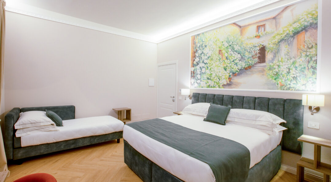 Triple room with a green upholstered double bed and a single bed, featuring a large floral painting above the headboard.