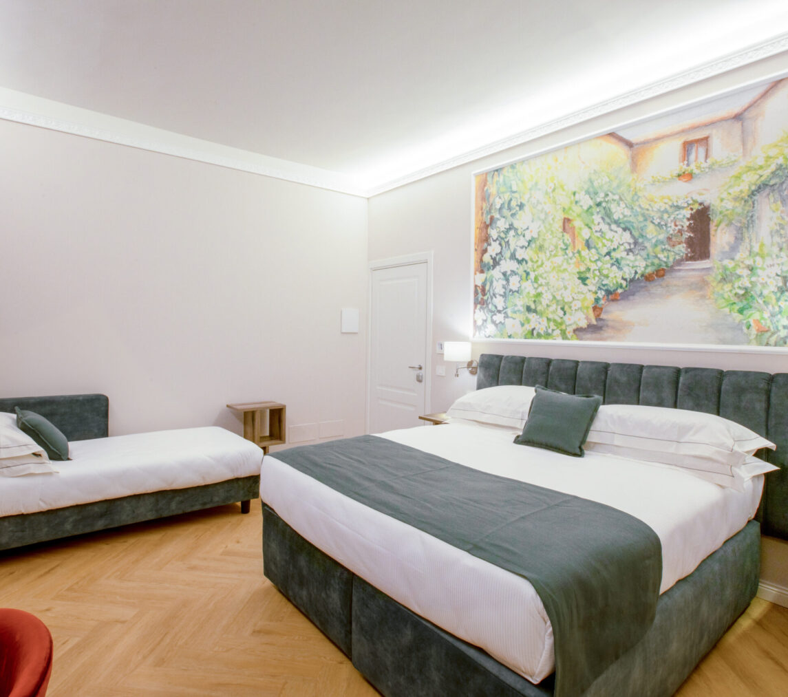 Camera tripla con letto matrimoniale e letto singolo, entrambi con rivestimento verde, e grande quadro floreale sopra la testiera.