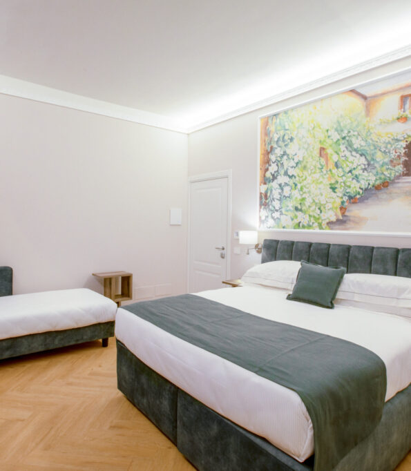 Triple room with a green upholstered double bed and a single bed, featuring a large floral painting above the headboard.