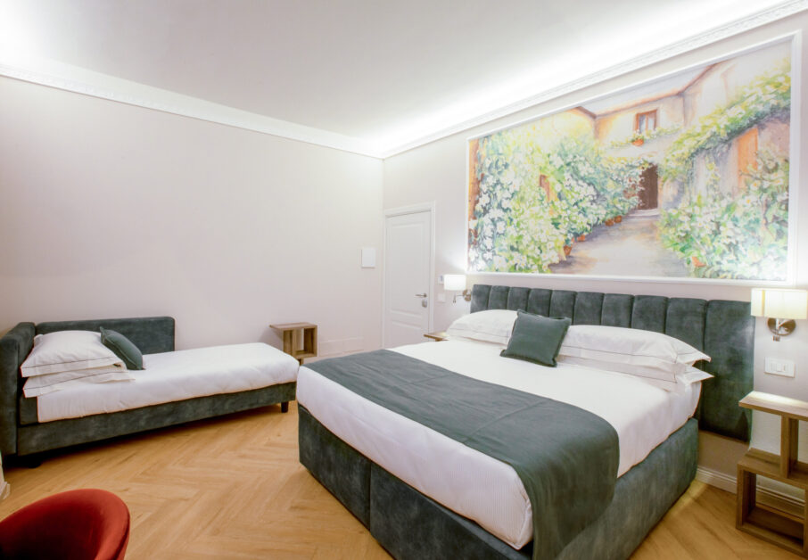Triple room with a green upholstered double bed and a single bed, featuring a large floral painting above the headboard.