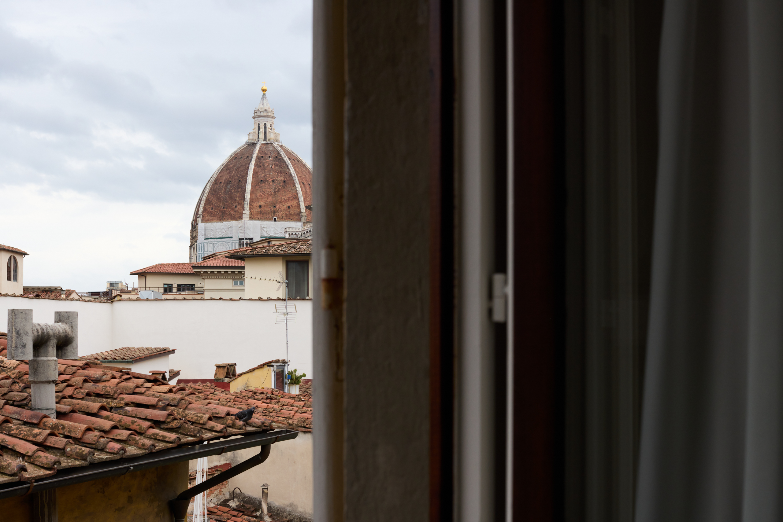 Vista parziale della Cupola del Duomo di Firenze attraverso una finestra, con i tetti in terracotta del centro storico in primo piano.