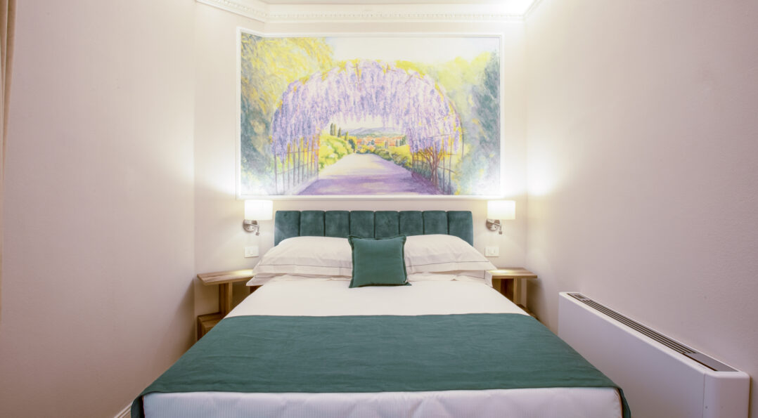 Camera singola con letto matrimoniale alla francese, testata verde e grande affresco sopra il letto raffigurante un tunnel di glicine in fiore.