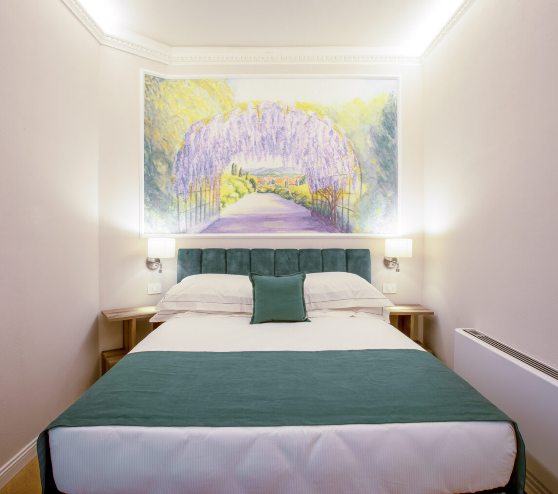 Camera singola con letto matrimoniale alla francese, testata verde e grande affresco sopra il letto raffigurante un tunnel di glicine in fiore.