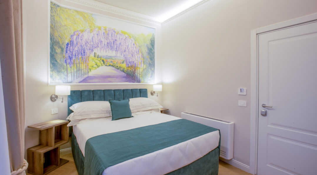 Bright single room with a French bed, teal headboard, and a large decorative painting of a wisteria pergola.