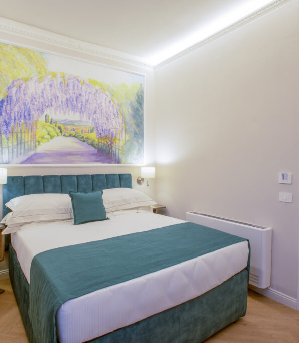 Bright single room with a French bed, teal headboard, and a large decorative painting of a wisteria pergola.