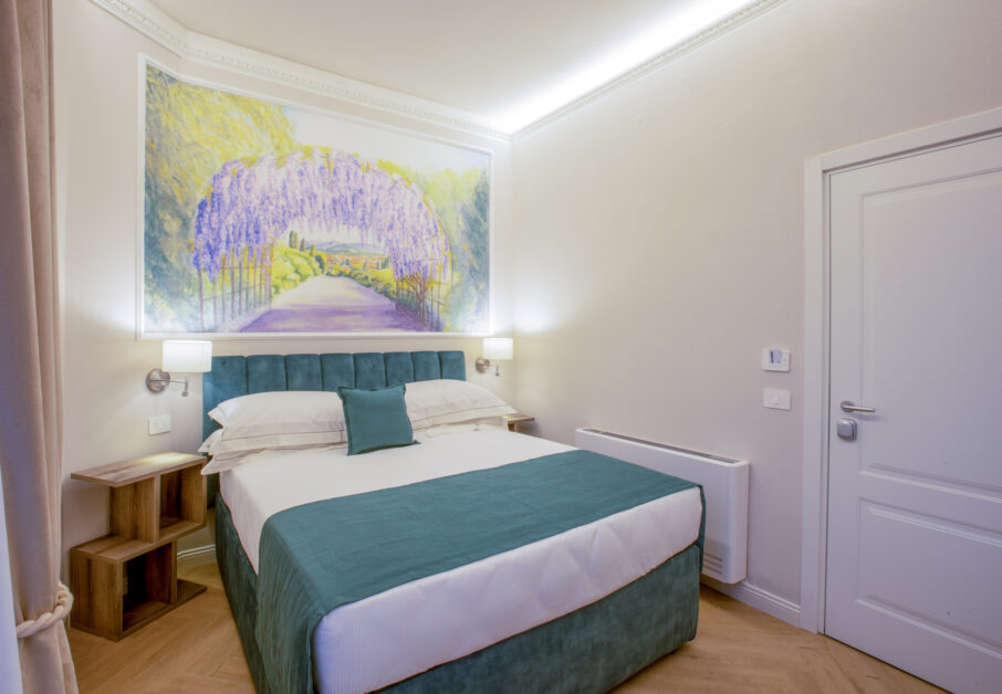 Bright single room with a French bed, teal headboard, and a large decorative painting of a wisteria pergola.