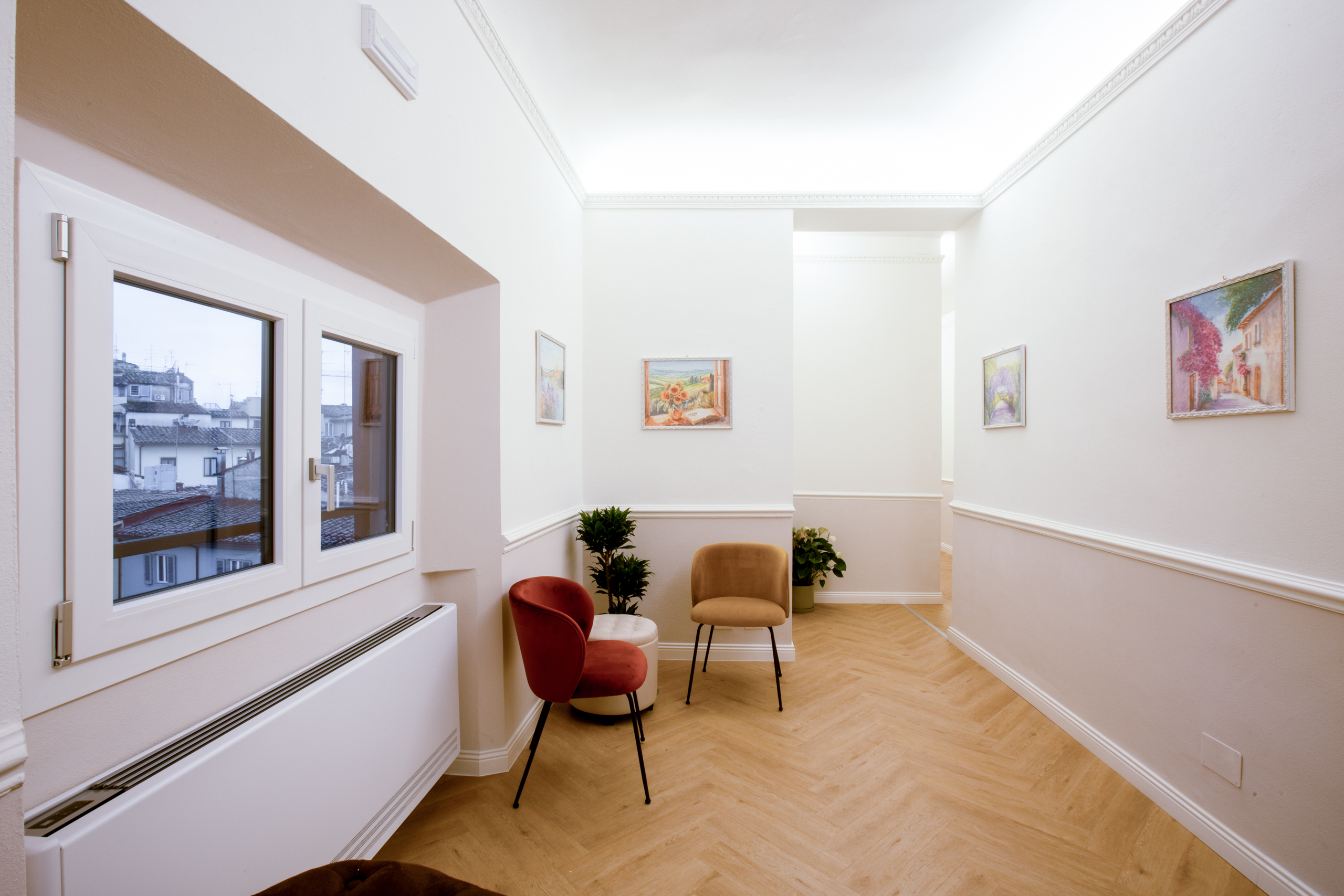 Piccola area comune dell’Hotel Settefiori con sedute colorate, quadri floreali e finestra con vista sui tetti del centro storico di Firenze.