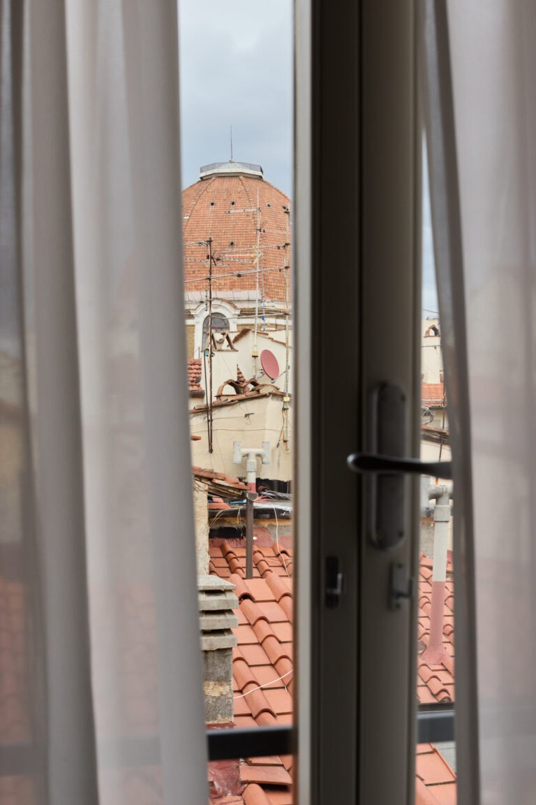 View of Florence’s Duomo seen through a window with sheer curtains, with terracotta rooftops in the foreground.